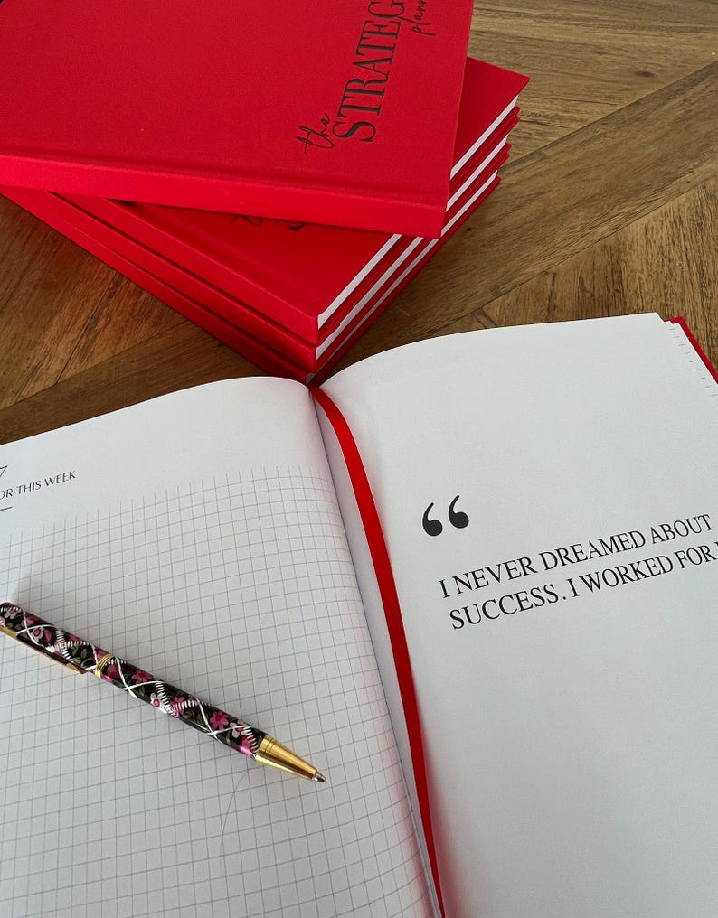 May include: Red hardcover planner with the text "the STRATEGIC planner" stacked on top of each other. An open planner with a quote and a floral pen are on the right. The quote reads, "I NEVER DREAMED ABOUT SUCCESS. I WORKED FOR".