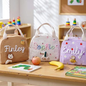 Pode incluir: Três lancheiras de veludo cotelê com alças superiores e fechos de zíper. A bolsa bege apresenta o nome Finley e um patch de leão. A bolsa branca apresenta o nome Sophie e um patch de cachorro. A bolsa roxa apresenta o nome Emily e um patch de abelha.