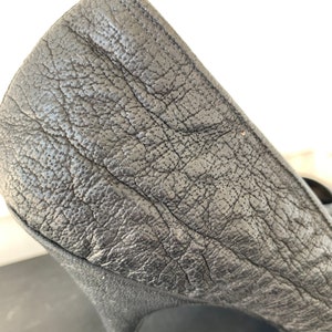 May include: Close-up of the back of a black leather high-heeled pump shoe.