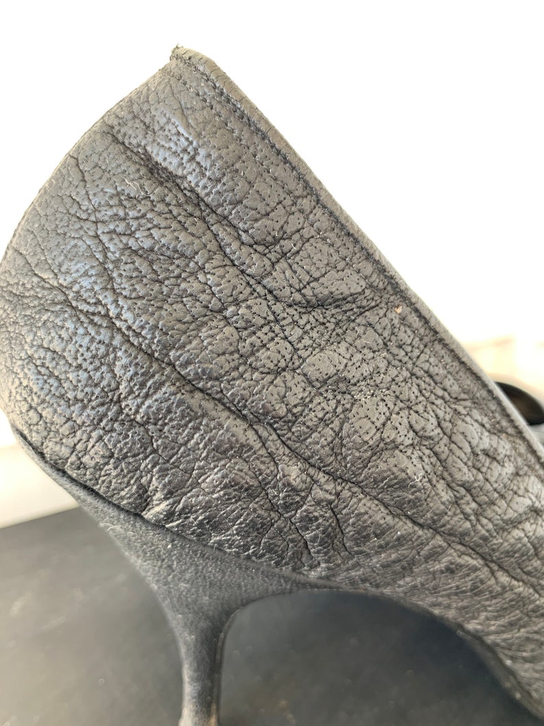 May include: Close-up of the back of a black leather high-heeled pump shoe.