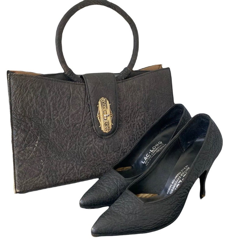 May include: A black leather handbag with a gold clasp and a matching pair of black leather shoes with a pointed toe and stiletto heels. The shoes have the text "LAC-LONG" printed on the insole.