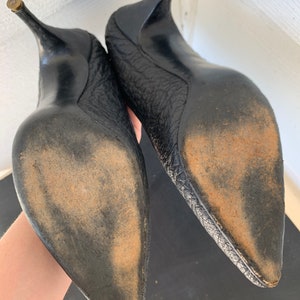 May include: A pair of black leather high-heeled shoes with pointed toes. The shoes have a textured leather upper and a worn leather sole.