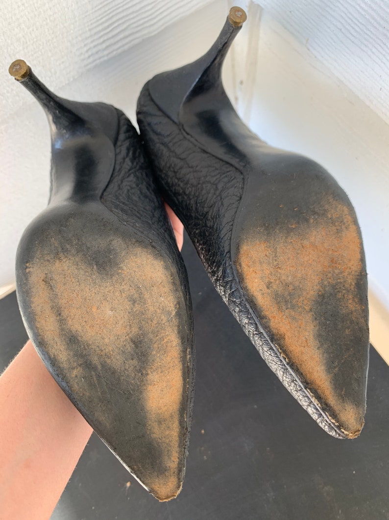 May include: A pair of black leather high-heeled shoes with pointed toes. The shoes have a textured leather upper and a worn leather sole.