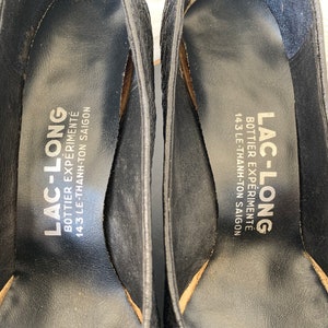 May include: Close-up of the inside of a black leather shoe with the text "LAC-LONG BOTTIER EXP&Eacute;RIMENT&Eacute; 143 LE-THANH-TON SAIGON" printed on the insole.