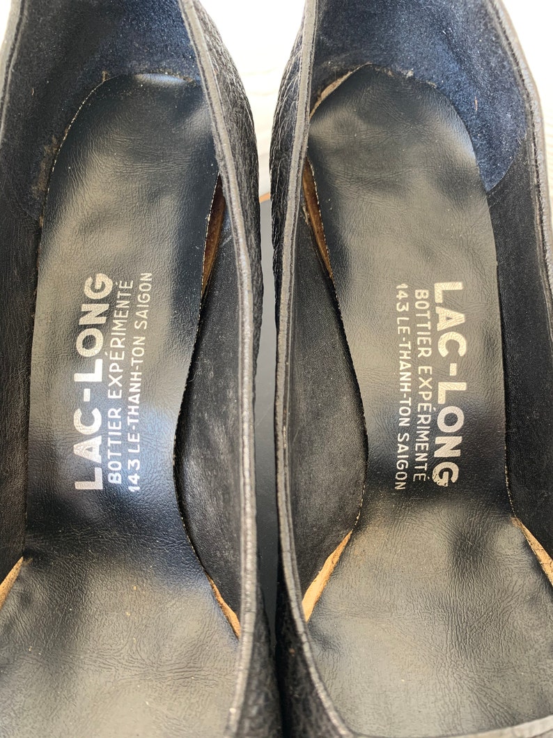 May include: Close-up of the inside of a black leather shoe with the text "LAC-LONG BOTTIER EXP&Eacute;RIMENT&Eacute; 143 LE-THANH-TON SAIGON" printed on the insole.