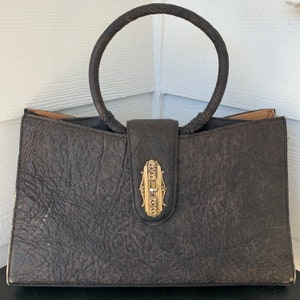 May include: A vintage brown leather handbag with a unique gold clasp and a circular top handle.