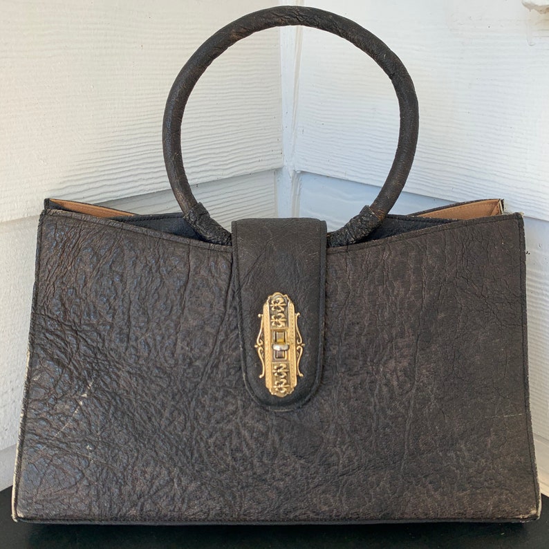 May include: A vintage brown leather handbag with a unique gold clasp and a circular top handle.
