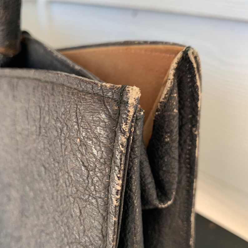 May include: Close-up of a black leather tote bag with a brown leather lining. The bag has a worn, distressed look, with visible stitching and creases.