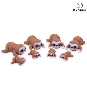 Puede incluir: Una colección de siete figuras de perezosos marrones y blancos de varios tamaños, con cuerpos redondeados, ojos oscuros y parches faciales claros. Las figuras están dispuestas en grupo, con el texto KYNS3D visible en la esquina superior derecha.