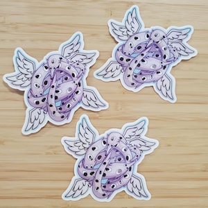 May include: Three stickers featuring a stylized, winged creature with multiple eyes and a coiled body. The stickers have a light purple and white color scheme with blue accents. The wings are outlined in blue.