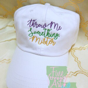 May include: White baseball cap with the text "Throw Me Something Mister" embroidered in purple, green, and gold. The cap has a Louisiana state outline with the text "Fine Thread Art" in pink and green.