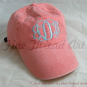 May include: Coral colored baseball cap with a sky blue embroidered monogram. The monogram is a script font with the letters "E.D.B."