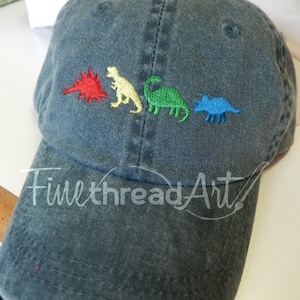 May include: A dark green, distressed, cotton baseball cap with an embroidered design of four dinosaurs in different colors: red, yellow, green, and blue. The dinosaurs are arranged in a line, walking from left to right. The text "FinethreadArt!" is embroidered on the front of the cap.