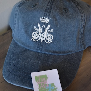 May include: A blue denim baseball cap with white embroidery of a crown and the letters "M" and "A". The cap is embroidered with the text "Fine Thread Art Embroidery" and a website address.