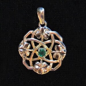 May include: A silver pendant with an intricate floral design. The pendant features a central green gemstone and is suspended from a small loop. The design is symmetrical and detailed, with a polished finish.