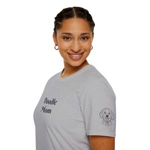 Könnte beinhalten: Hellgraues T-Shirt mit dem Aufdruck "Doodle Mom" auf der Vorderseite. Auf dem Ärmel befindet sich eine kleine schwarz-weiße Doodle-Hunde-Grafik. Das Shirt besteht aus einem weichen Material.