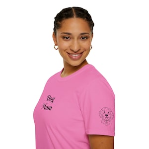 Könnte beinhalten: Ein pinkfarbenes T-Shirt mit dem Aufdruck "Dog Mom" auf der Vorderseite. Auf dem Ärmel befindet sich eine kleine Hundeillustration. Das T-Shirt hat eine einfarbige rosa Farbe.