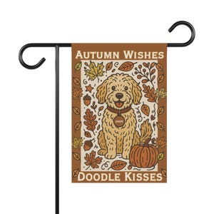 Könnte beinhalten: Eine braune und cremefarbene Gartenflagge mit einem schwarzen Metallständer. Die Flagge zeigt einen Cartoon-Doodle-Hund mit einem Kürbis und Herbstblättern. Auf der Flagge steht "Autumn Wishes" und "Doodle Kisses". Der Hund hat ein Namensschild mit "Annie".