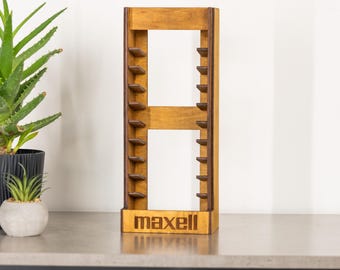May include: A wooden media storage rack shaped like the letter "A". The rack is made of light brown wood with small shelves for storing media. The word "maxell" is printed on the base of the rack.