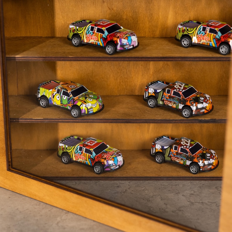 May include: A wooden display case with six colorful toy trucks. Each truck has a unique graffiti-style design with various colors. The trucks are displayed on separate shelves within the case.