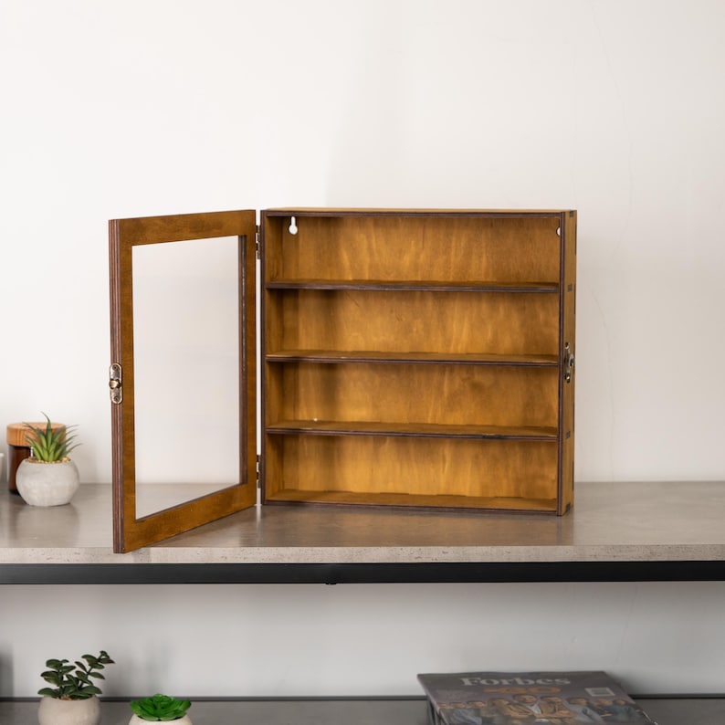 May include: A wooden display cabinet with a glass door, featuring four shelves. The cabinet is stained in a warm brown color, with the door open to the left. The cabinet is designed to be mounted on a wall.