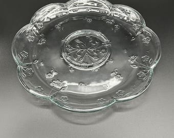 May include: Clear glass serving platter with a scalloped edge and embossed floral design. The center features a raised floral pattern. The platter is round with a slightly raised center and is ideal for serving appetizers or desserts.