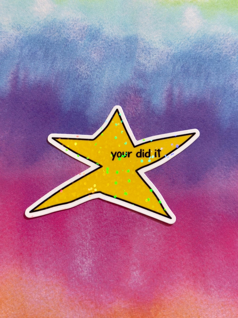 以下が含まれることがあります： 手書きフォントで「your did it」と書かれた黄色の星型ステッカー。星には白い縁取りがあり、キラキラで満たされています。背景は紫、青、ピンクの水彩画です。