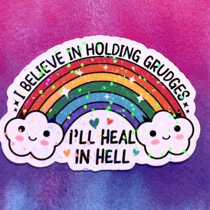 Puede incluir: Una pegatina con un diseño de arcoíris y el texto "I BELIEVE IN HOLDING GRUDGES" en la parte superior y "I'LL HEAL IN HELL" en la parte inferior. El arcoíris tiene purpurina y gráficos de nubes sonrientes, sobre un fondo colorido.