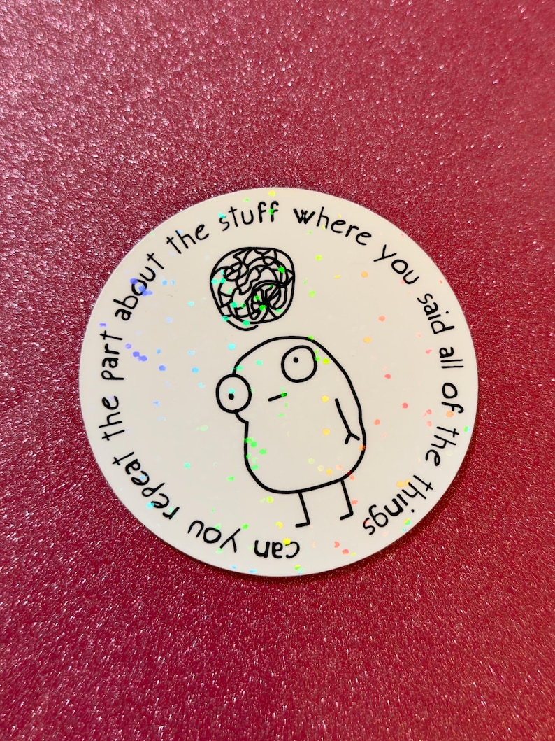 May include: A round white sticker with a cartoon figure and the text "can you repeat the part about the stuff where you said all of the things". The sticker has a holographic effect and is on a red surface.