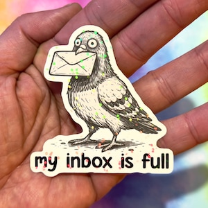 Op de afbeelding: Een sticker met een cartoon duif die een envelop in zijn bek houdt. De duif is zwart-wit met glitteraccenten. De tekst "my inbox is full" staat eronder.