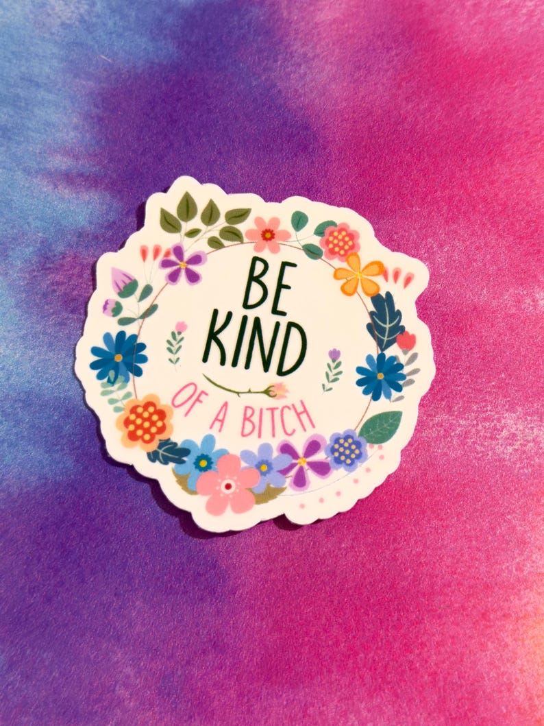 May include: A white sticker with a floral wreath design. The text "BE KIND OF A BITCH" is in the center. The sticker features various colorful flowers and green leaves, set against a vibrant pink and purple background.