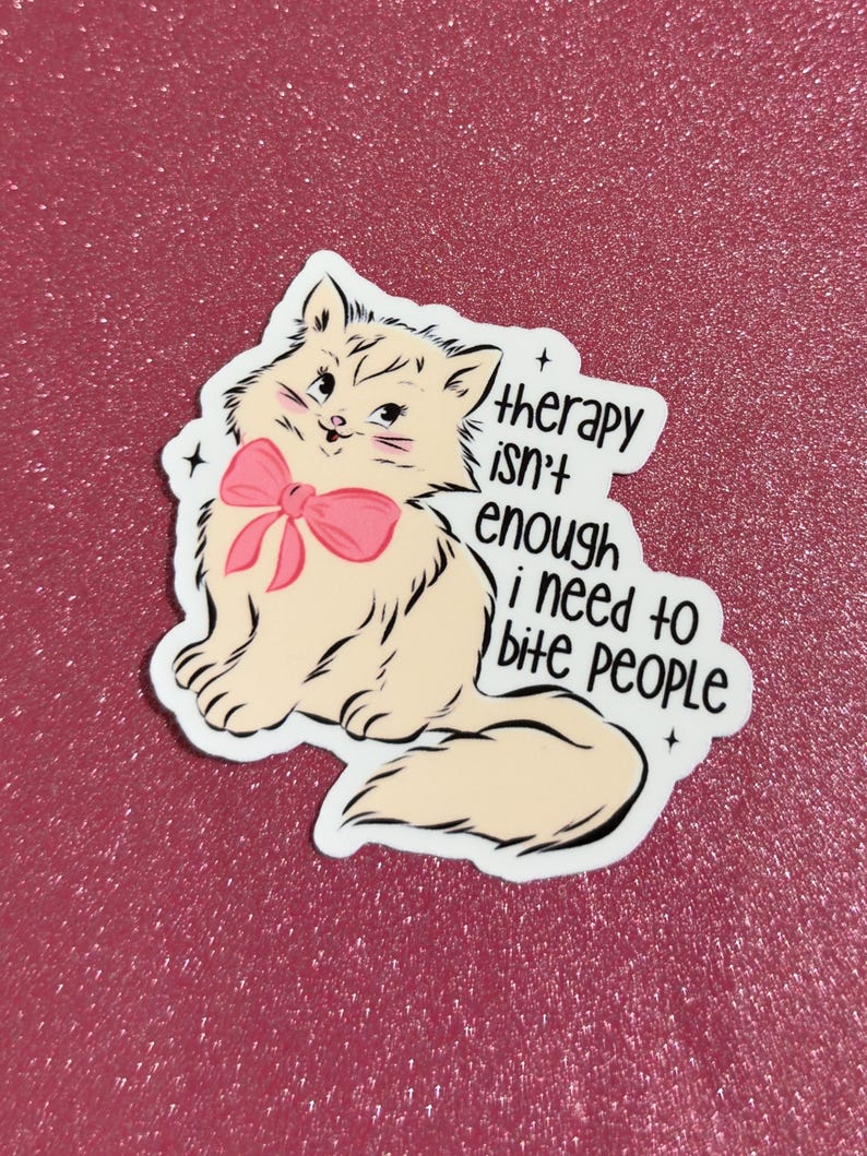 May include: A sticker featuring a cartoon cat with a pink bow and the text "therapy isn't enough i need to bite people." The cat is light tan with black outlines and is set against a pink glitter background.