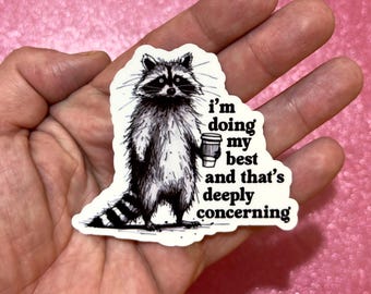 May include: A black and white sticker featuring a raccoon holding a coffee cup. The text on the sticker reads "I'm doing my best and that's deeply concerning."
