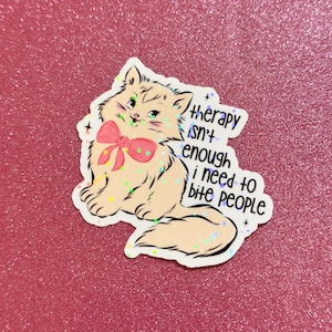 May include: A sticker featuring a cartoon cat with a pink bow, green eyes, and the text "therapy isn't enough i need to bite people." The sticker has a glittery, holographic effect and is on a pink background.