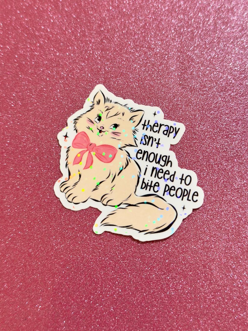 May include: A sticker featuring a cartoon cat with a pink bow, green eyes, and the text "therapy isn't enough i need to bite people." The sticker has a glittery, holographic effect and is on a pink background.