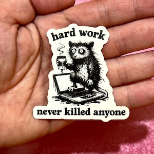 May include: A black and white sticker featuring an opossum holding a coffee cup and sitting on a laptop. The text "hard work" is above the opossum, and "never killed anyone" is below.
