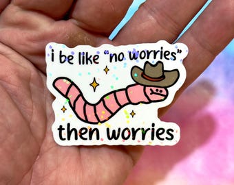 May include: A sticker featuring a pink worm wearing a cowboy hat. The text says "i be like 'no worries' then worries". The sticker has a holographic glitter effect and star accents.