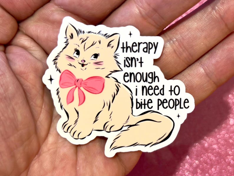 May include: A sticker featuring a cartoon cat with a pink bow, with the text "therapy isn't enough I need to bite people." The cat is cream-colored with black outlines and whiskers. The sticker has a white border and black stars.