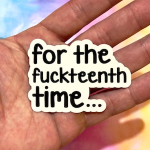 Op de afbeelding: Een witte sticker met zwarte tekst die luidt "for the fuckteenth time...". De sticker wordt in een hand gehouden tegen een kleurrijke, vage achtergrond.