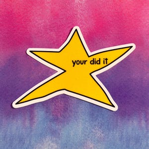 以下が含まれることがあります： 黒いアウトラインと「your did it」という黒い文字が入った黄色の星型のステッカー。ステッカーは、ピンク、紫、青のタイダイの背景に配置されています。