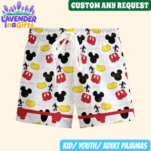 A pair of white shorts with a repeating pattern of Mickey Mouse and other cartoon characters printed on them.