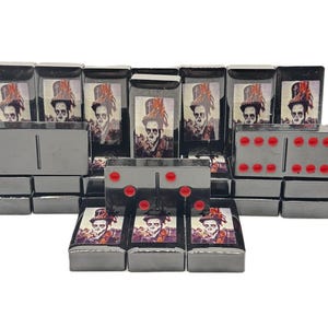 May include: A set of black dominoes with a unique design. Each domino features a metallic finish and a printed image of a skeleton wearing a top hat. The dominoes have red dots and are arranged on a white surface.