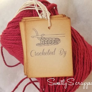 May include: A close-up of a red yarn ball with a brown tag attached. The tag has a hand-drawn illustration of a crochet stitch and the text "Crocheted By Sweetly Scrapped".