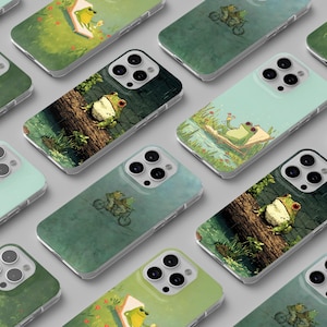 Pode incluir: Uma coleção de capas de telefone com várias ilustrações de sapos. Os designs incluem um sapo num tronco, andando de bicicleta e relaxando numa jangada. As capas apresentam fundos verdes e azuis.