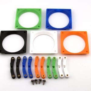 May include: A collection of five square frames with circular cutouts in green, blue, black, white, and orange. Below are ten curved brackets in matching colors, each with embedded metal inserts, and four small metal screws for assembly.