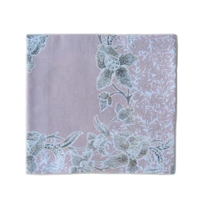 Op de afbeelding: Een vierkant, lavendelkleurig textiel met een bloemenontwerp. Het ontwerp toont grote, gestileerde bloemen en bladeren in grijstinten en wit, met een gedetailleerde, patroonachtergrond. De randen zijn afgewerkt met een lichtblauwe rand.