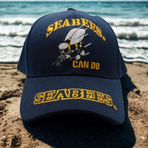 以下が含まれることがあります： SEABEESとCAN DOの黄色い刺繍文字が入ったネイビーの野球帽。フロントパネルには、道具を持った蜂のキャラクターの刺繍が施されています。つばの部分にも黄色でSEABEESという文字が刺繍されています。
