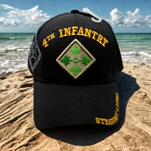 Könnte beinhalten: Schwarze Baseballkappe mit goldfarbener Stickerei "4th Infantry". Sie hat ein grünes und beiges Diamanten-Patch und den goldenen Schriftzug "Steadfast & Loyal". Ein weißes Etikett ist an der Kappe befestigt.