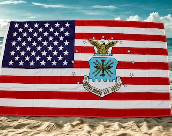 Puede incluir: Bandera estadounidense con el emblema de la Fuerza Aérea de los Estados Unidos. La bandera presenta franjas rojas y blancas, un campo azul con estrellas blancas y el emblema de la Fuerza Aérea en el centro. La bandera se muestra en una playa de arena con el océano al fondo.