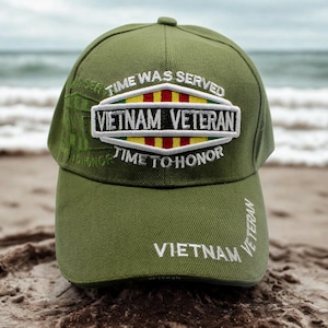 Puede incluir: Gorra de béisbol verde oliva de veterano de Vietnam con texto bordado y parche. El parche dice "Vietnam Veteran" y "Time to Honor". La gorra está en una playa de arena con el océano al fondo.